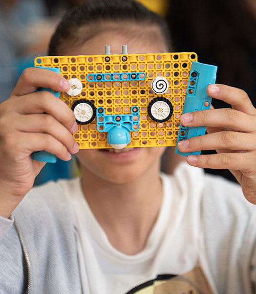 Ein Kind hält ein selbstgebautes Spielzeug vor dessen Gesicht in die Kamera. © Lena Mucha / Save the Children