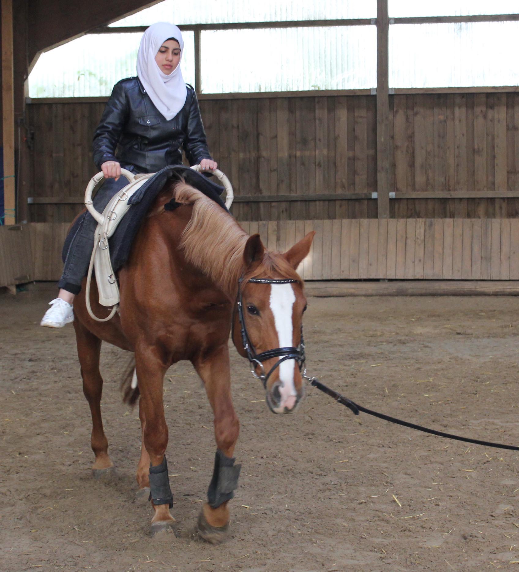 Mädchen mit Kopftuch reitet auf Pferd an der Longe