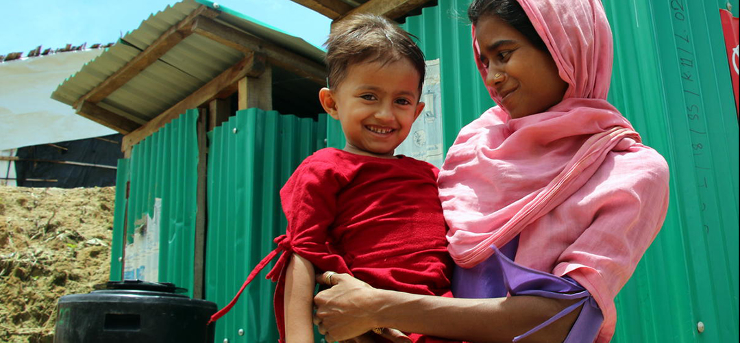 Zaheeda* (3) und ihre Mutter Minora* (25) stehen in einem Flüchtlingslager in Cox's Bazar vor einer Toilette, die von Save the Children gebaut wurde. © Daphnee Cook / Save the Children