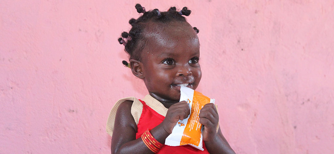 Ein kleines Mädchen aus dem Sudan hält eine Packung therapeutische Spezialnahrung in der Hand. 