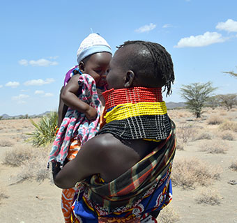 Eine kenianische Mutter hält ihr kleines Baby hoch und küsst es ins Gesicht. 