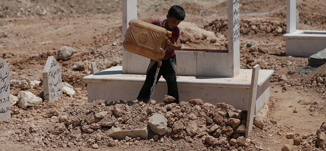 Ein acht Jahre alter Junge in Syrien bewässert ein frisches Grab auf einem Friedhof mit einem Wasserkanister. 