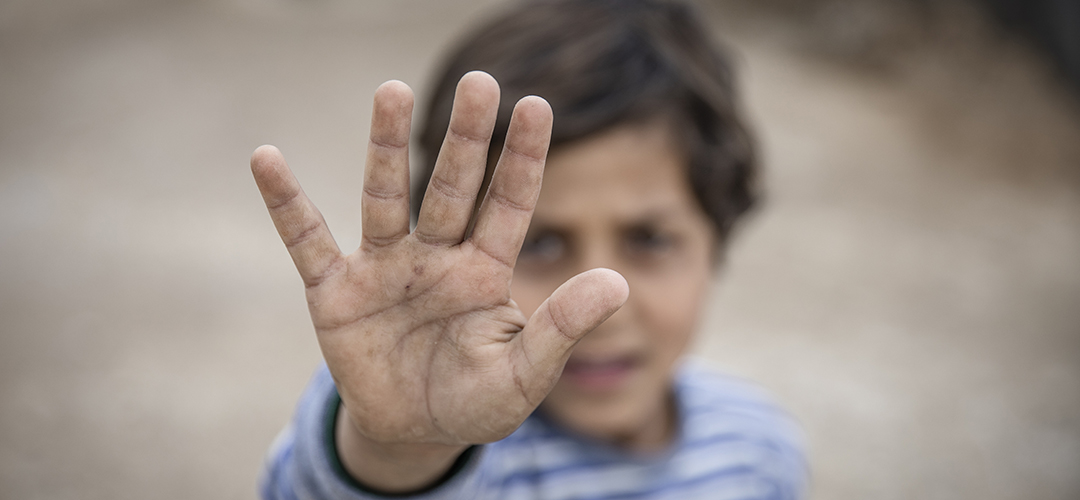 Ein syrisches Kind hält die rechte Hand zu einem Stop-Zeichen nach oben gestreckt. 