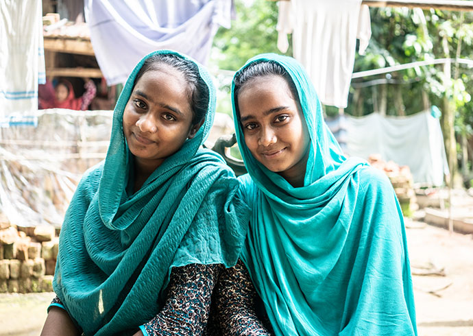 Zwei lächelnde Mädchen vor ihrem zu Hause in Bangladesch.