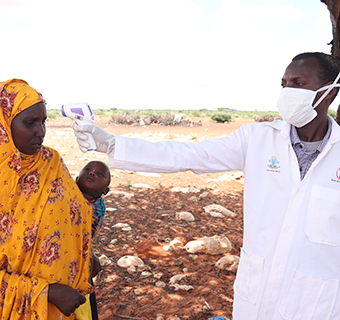 Ein Gesundheitshelfer von Save the Children in Somalia misst bei einer Frau und ihrem Kind Fieber als Maßnahme gegen die Ausbreitung des Corona-Virus. © Abdirahman Mohamed / Save the Children