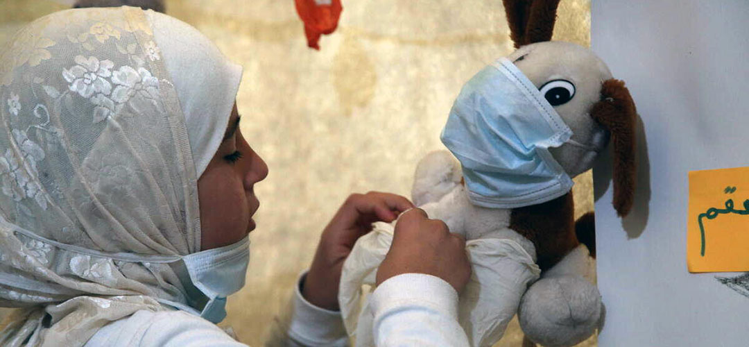 Salam* setzt ihrem Teddy eine Maske auf, um ihn symbolisch vor dem Coronavirus zu schützen. © Save the Children