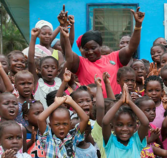 Die Hebamme Alice feiert inmitten der Kinder, die nach ihr benannt wurden, vor einem von Save the Children gebauten Krankenhaus in Liberia. © Hanna Adcock / Save the Children