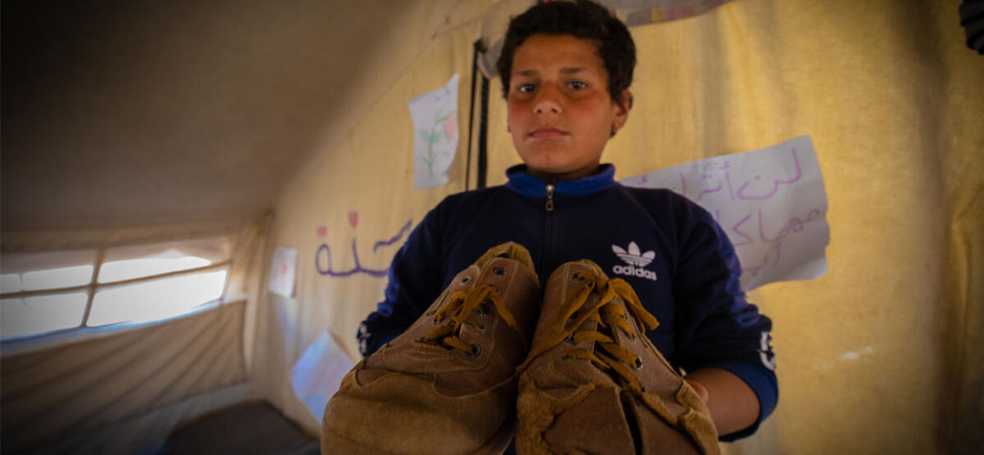 Der 13-jährige Yousef* hält die Schuhe seines verstorbenen älteren Bruders in den Händen.