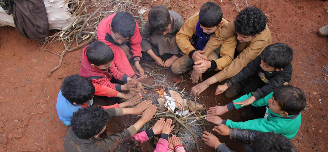 Syrische Kinder auf der Flucht halten sich um ein Feuer herum warm. Sie alle teilen ein gemeinsames Schicksal: Eine Kindheit im Krieg. 