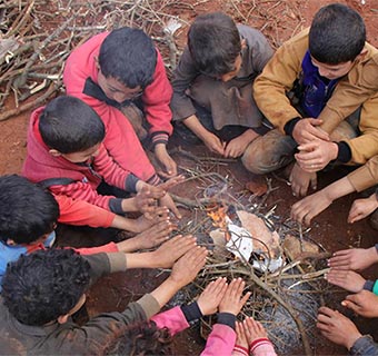 Syrische Kinder auf der Flucht halten sich um ein Feuer herum warm. Sie alle teilen ein gemeinsames Schicksal: Eine Kindheit im Krieg. 