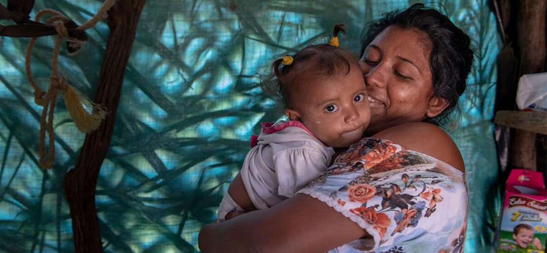 Anastonia* umarmt ihre anderthalb Jahre alte Tochter Luz* in ihrem Zuhause in einer Siedlung in Maicao, Kolumbien.