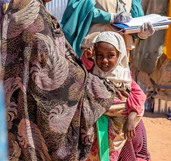 Die kleine Hamda lebt in einem Camp für Geflüchtete in Somalia, Afrika. Hier wird sie von der Save the Children-Gesundheitshelferin Muna versorgt, nachdem bei ihr eine Form der Unterernährung festgestellt wurde. Zudem erhält ihre Familie Unterstützung dabei, sich vor Covid-19 zu schützen.