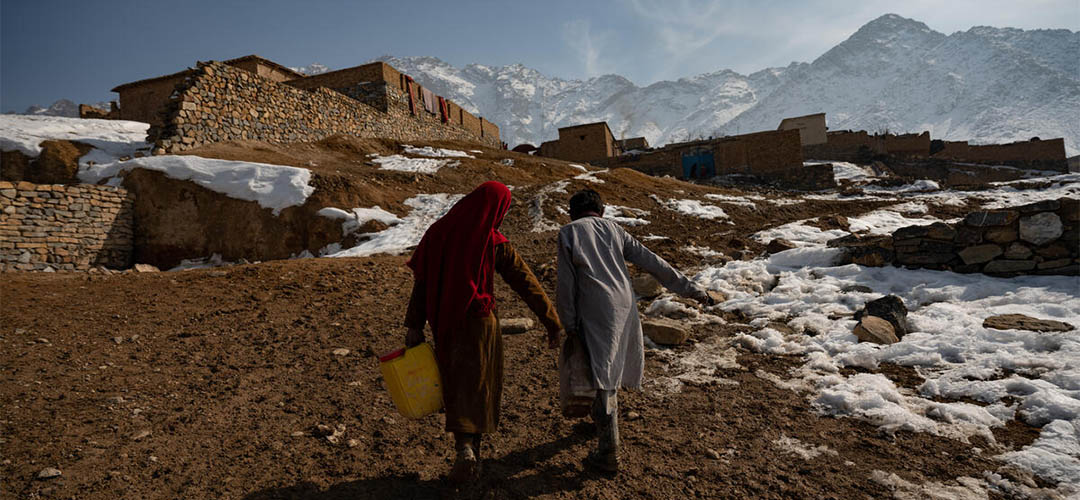 Zwei Kinder in Afghanistan, die im Schnee Wasserkanister tragen.