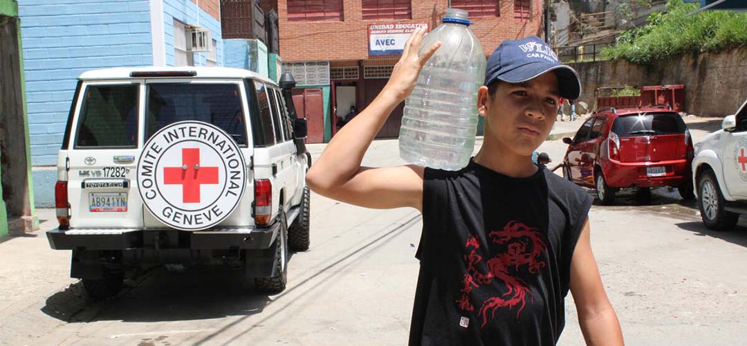 Luis* trägt eine 5-Liter-Wasserflasche zu seinem Haus, nachdem er sie am Brunnen aufgefüllt hat.