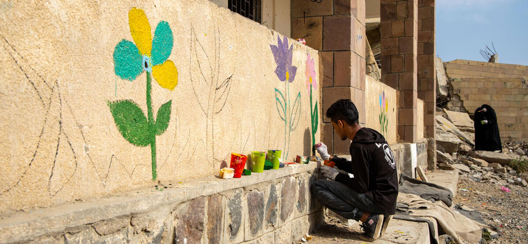 Junge malt Blumen auf zerstörte Schule im Jemen.