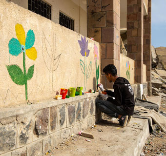 Junge malt Blumen auf zerstörte Schule im Jemen. 