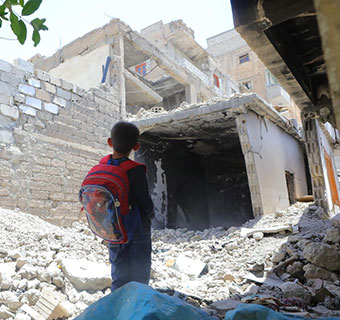 Ein syrischer Junge steht vor zerstörten Gebäuden in Al Raqqa. © Muhannad Khaled / Save the Children