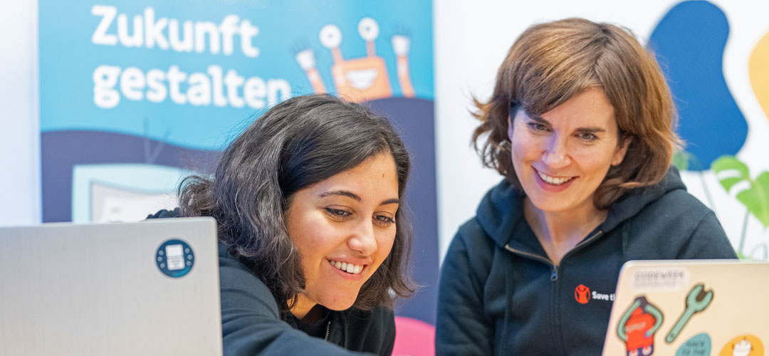 Zwei Mitarbeiterinnen im MakerLabs-Projekt schauen zusammen lächelnd in einen Laptop. © Mauro Bedoni / Save the Children