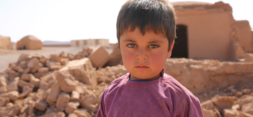 Ein Junge in Afghanistan steht vor den Trümmern seines Hauses, das bei einem Erdbeben zerstört wurde. © Atabek Khadim / Save the Children