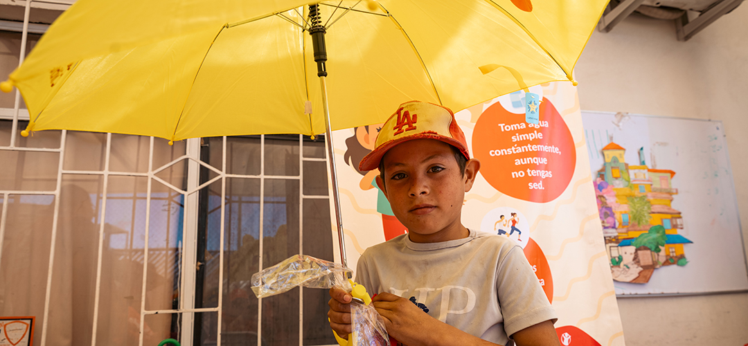 Ein Kind mit einem Sonnenschirm aus unserem Hitzeschutz-Kit. © Miguel Vera / Save the Children Mexiko Ein Kind steht unter einem gelben Sonnenschirm