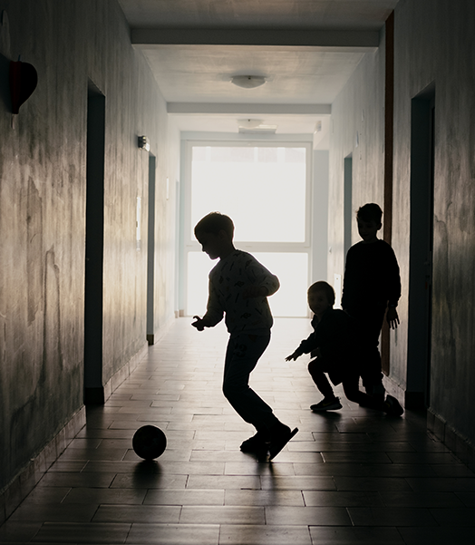 Symbolbild: Kinder in einer Unterkunft für Geflüchtete spielen Fußball. © Save the Children Drei Kinder, die in einem dunklen Flur Fußball spielen.