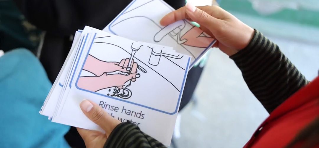 Wissen schützt: Humanitäre Helfer*innen geben eine Hygieneschulung. © Save the Children Eine Mitarbeiterin hält Informationsmaterial für eine Hygieneschulung in der Hand
