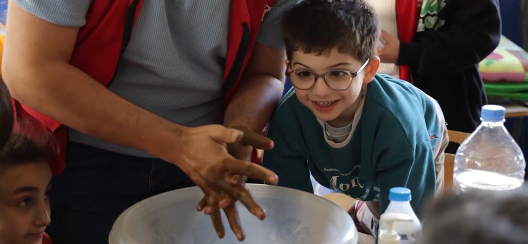 Ein Beispiel für humanitäre Hilfe: Kinder in einer Unterkunft lernen richtiges Händewaschen. © Save the Children Ein Kind schaut zu, wie Hände gewaschen werden