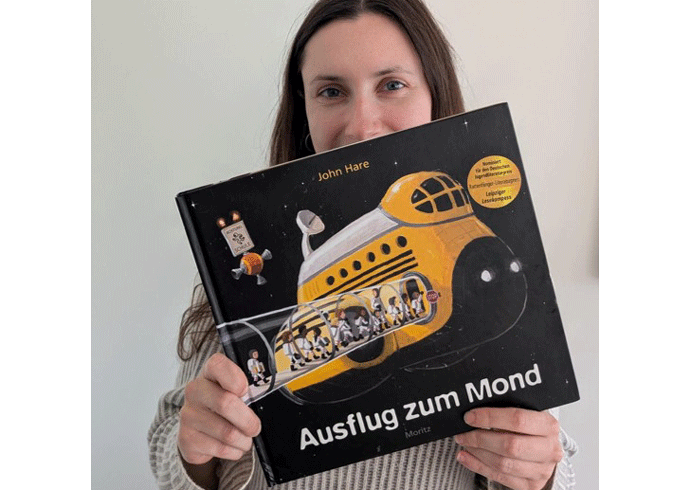 Eine Frau hält ein Buch in die Kamera mit dem Titel: Ausflug zum Mond