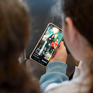 Makerlabs kinder handy CH11448637 320x320 Zwei Kinder, die von hinten zu sehen sind, halten ein Smartphone in der Hand.