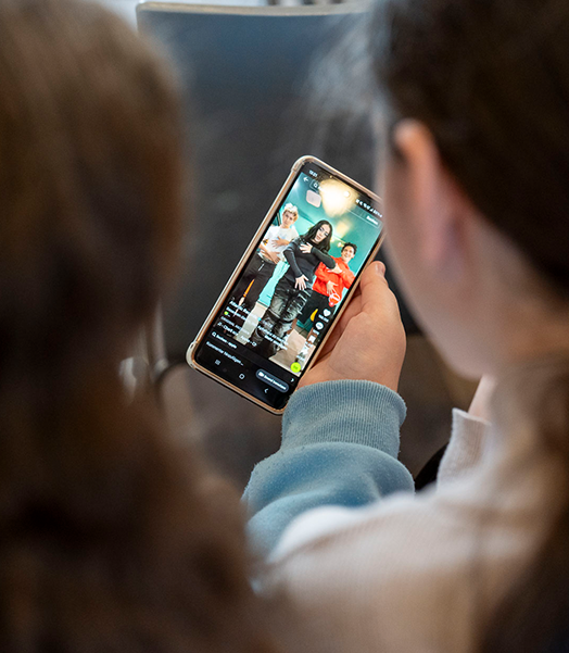 Zwei Kinder, die von hinten zu sehen sind, halten ein Smartphone in der Hand.