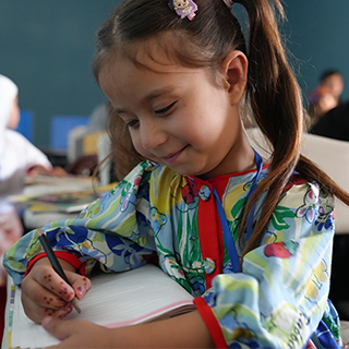 In Afghanistan unterstützt Save the Children geflüchtete Kinder beim Lernen. © Save the Children Ein lächelndes Mädchen, das mit einem Stift in ein Heft schreibt.