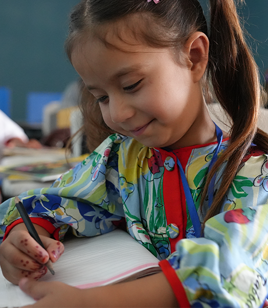 In Afghanistan unterstützt Save the Children geflüchtete Kinder beim Lernen. © Save the Children Ein lächelndes Mädchen, das mit einem Stift in ein Heft schreibt.