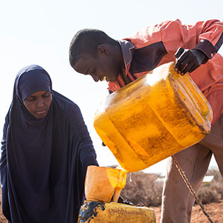 Mitarbeiter von Save the Children füllt Wasserbehälter einer Frau in Mogadishu