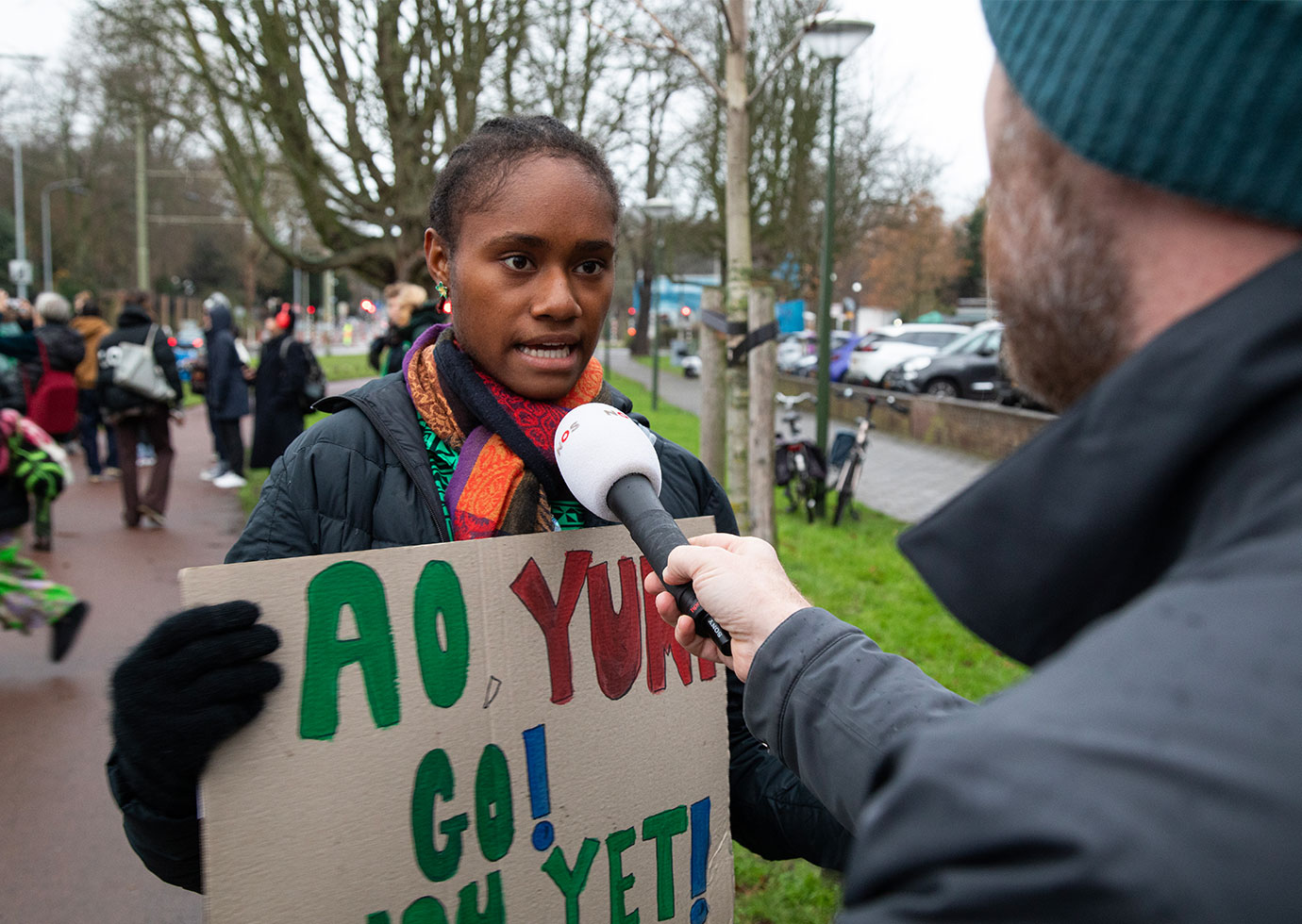 Vepaiamele, 15, gibt ein Interview vor dem Friedenspalast in Den Haag. © Tom Maguire / Save the Children Ein Mädchen mit einem Plakat in der Hand wird von einem Mann mit Mikrofon interviewt.