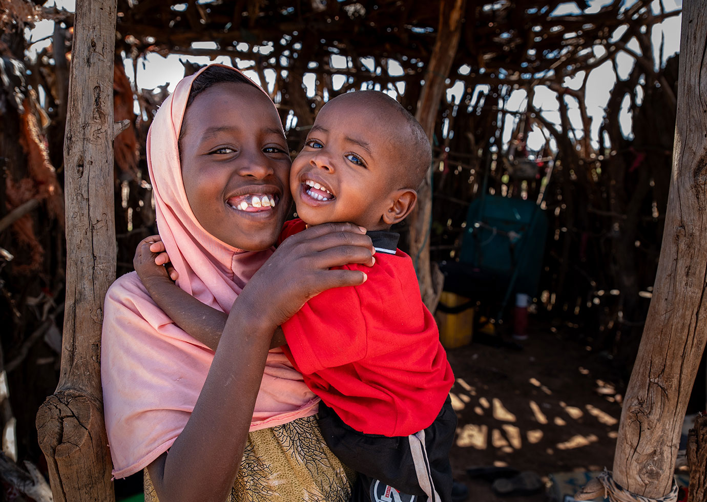 Faduma liebt ihren kleinen Bruder sehr. Als er mangelernährt war, machte sie sich große Sorgen um Abdi. © Mustafa Saeed / Save The Children Ein Mädchen hält einen kleinen Jungen auf dem Arm. Beide lachen in die Kamera.