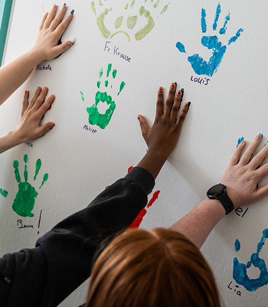Besuch eines MakerLabs in Dortmund: Seit ihrem Start 2019 zielen die Maker-Projekte von Save the Children darauf ab, die Teilhabe junger Menschen zu fördern. © Melissa Clement / Save the Children Mehrere Jugendliche machen Handabdrücke auf einer Wand.