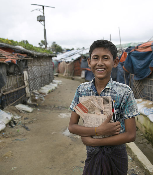 Ein lächelnder Junge trägt Zeitungen im Flüchtlingscamp in Cox's Bazar. 