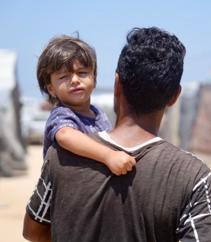 Ein Vater trägt sein Kind in einer Notunterkunft im Gazastreifen.