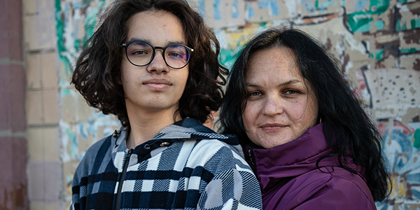 Oleksandr*, 15 Jahre, lebt in der Ukraine und träumt davon, Tanzlehrer zu werden. © Sacha Myers / Save the Children Ein Junge im Teenageralter mit braunen langen Haaren und Brille steht neben seiner Mutter.