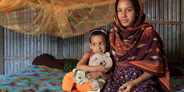 Tisha* wird bei der Geburt ihres zweiten Kindes Hilfe von Hebammen erhalten. © Fatima Tuj Johora / Save the Children Eine Mutter sitzt mit ihrer Tochter im Arm auf einem Bett.