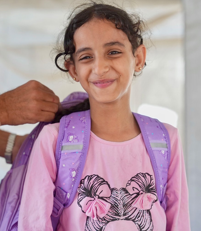 Dauerspenden helfen langfristig Kindern in Not weltweit. © Save the Children Ein lächelndes Mädchen bekommt einen Schulrucksack