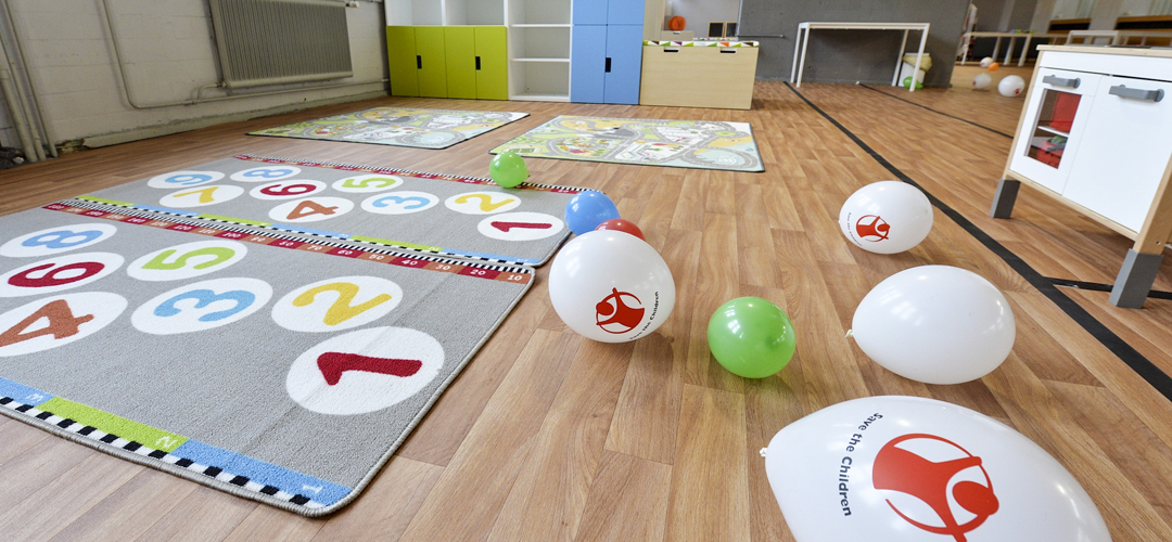 Ein Raum mit farbenfrohen Spielteppichen, einer Puppenküche und Luftballons.