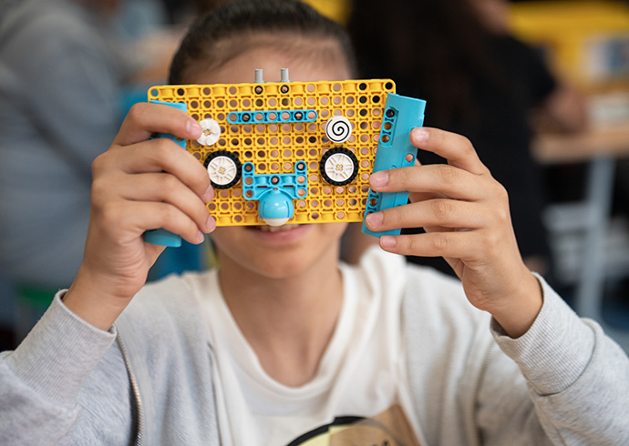 Bei einem Build the Change-Training im MakerLabs-Projekt haben jugendliche Peer-Trainer*innen Grundschulkinder beim Bauen mit LEGO Steinen und Programmieren von LEGO Spike Prime Robotern angeleitet. © Lena Mucha / Save the Children Ein Kind hält eine LEGO-Konstruktion vors Gesicht.