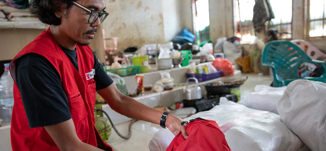 Ein Mann mit Save the Children-Weste hält einen Rucksack in der Hand.