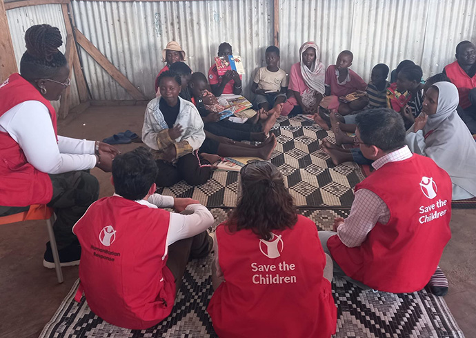 Besuch im Geflüchtetencamp Kakuma in Kenia. © Luis Pabon / Save the Children Kinder sitzen mit Mitarbeitenden von Save the Children im Kreis