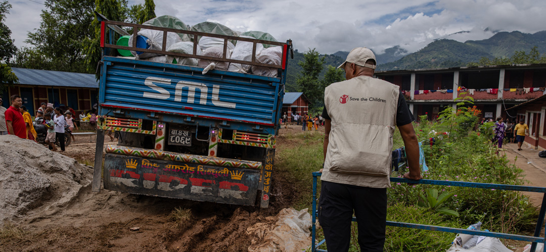 Hilfsgüter erreichen die Menschen per LKW, aber auch mit Drohnen. So ist Unterstützung auch dort möglich, wo anders kein Durchkommen ist. © Ulet Ifansasti / Save the Children Ein LKW fährt in Schräglage durch eine Schlamm-Piste. Ein Mann mit Save the Children-Weste beobachtet die Szene.