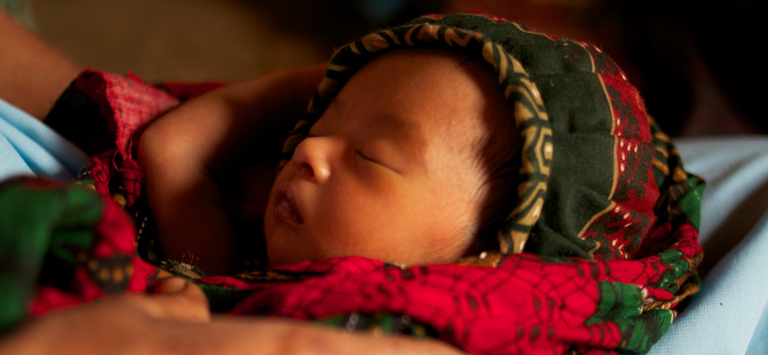Ein Baby ist in farbige Kleidung eingewickelt und schläft.