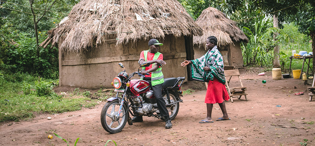 Ein Gesundheitshelfer auf seinem Motorrad begrüßt eine Frau. 