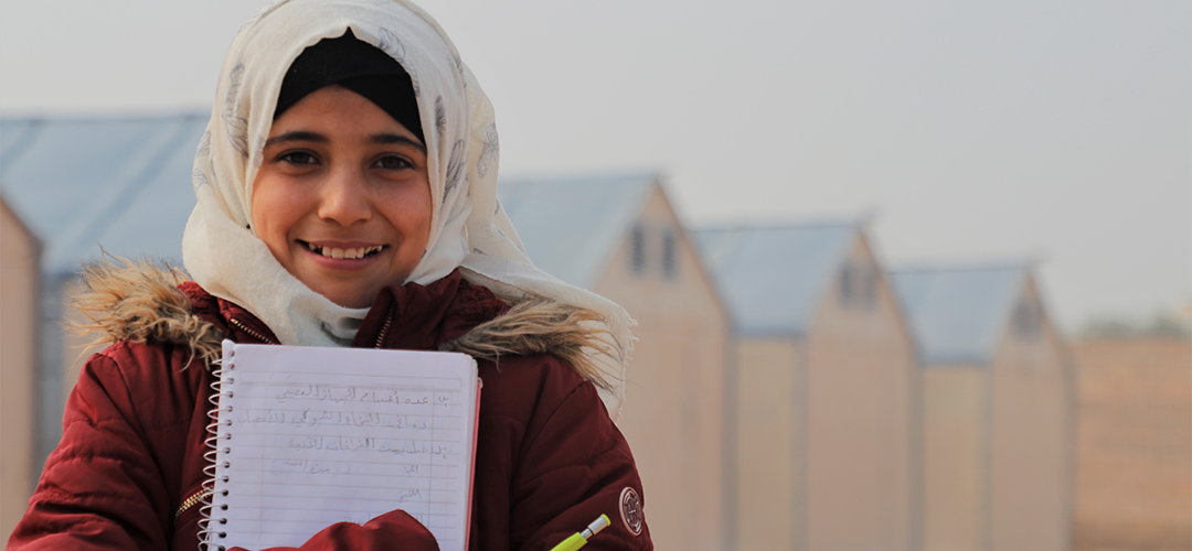 Ein Mädchen steht lächelnd mit Block und Stift in der Hand vor einer langen Reihe mit Zelten.
