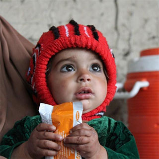 Ein kleiner Junge aus Afghanistan hält eine Packung Plumpynut in den Händen